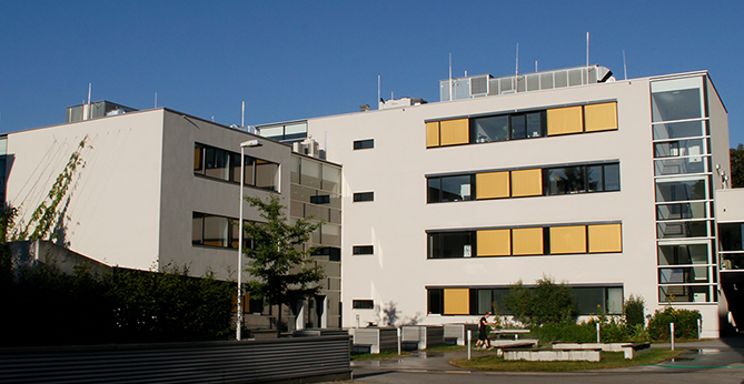 Modernes mehrgeschossiges Bürogebäude mit weißer Fassade, gelben Sonnenschutzelementen und verglastem Treppenhaus.