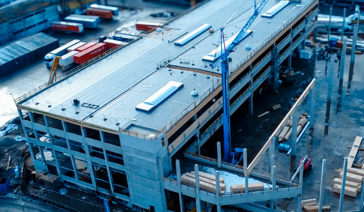 Drohnenaufnahme eines Gewerbebaus im Rohbau mit mehrgeschossiger Tragkonstruktion und angrenzender Hallenerweiterung.